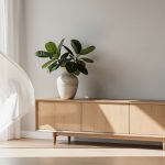 Salon lumineux décoré avec un buffet en bois clair, un vase en grès, une plante verte et des rideaux blancs semi-transparents.