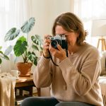 Une jeune photographe amateur prend une photo dans un salon chaleureux baigné de lumière naturelle.